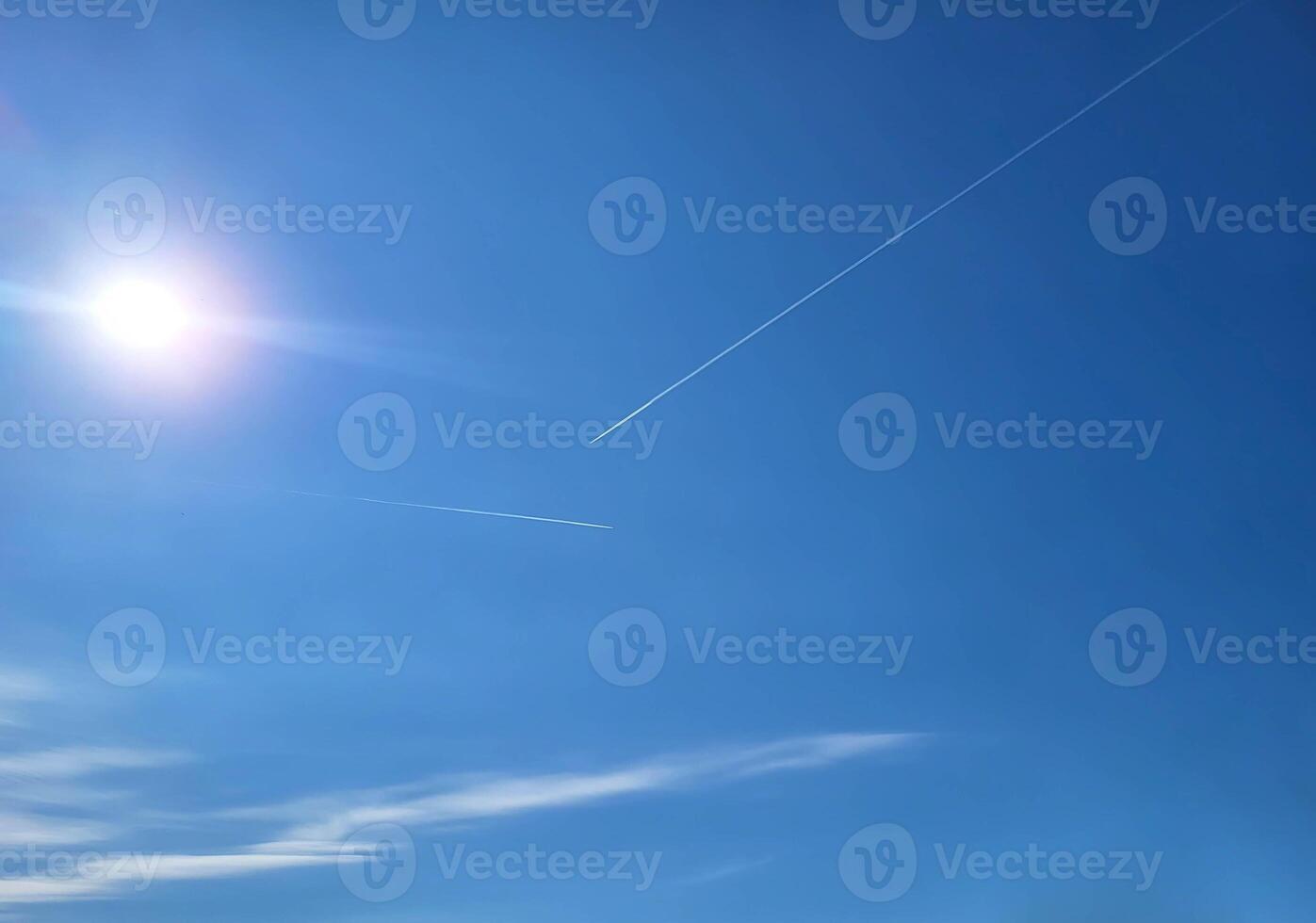 Blue sky, a glimmer of the sun, a trace of an airplane and clouds. photo