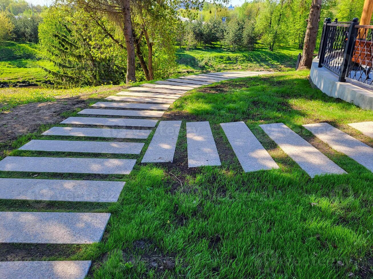 In the spring park, a path made of concrete rectangles is laid between the trees. The concept of landscaping and landscape design photo