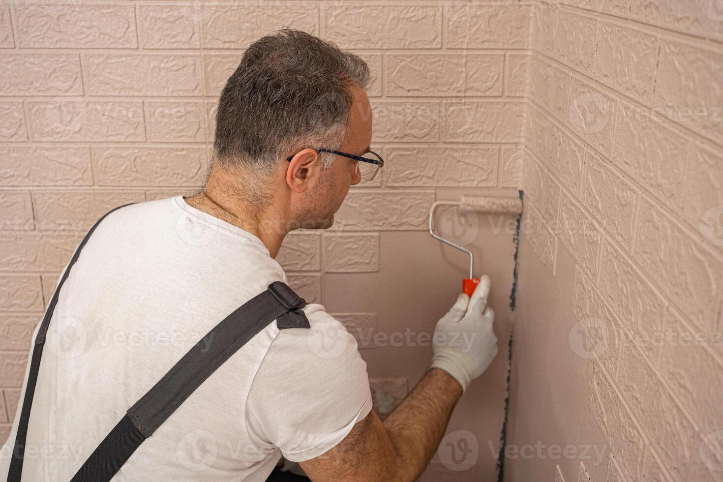 Man in a work suit paints a wall with a small roller photo