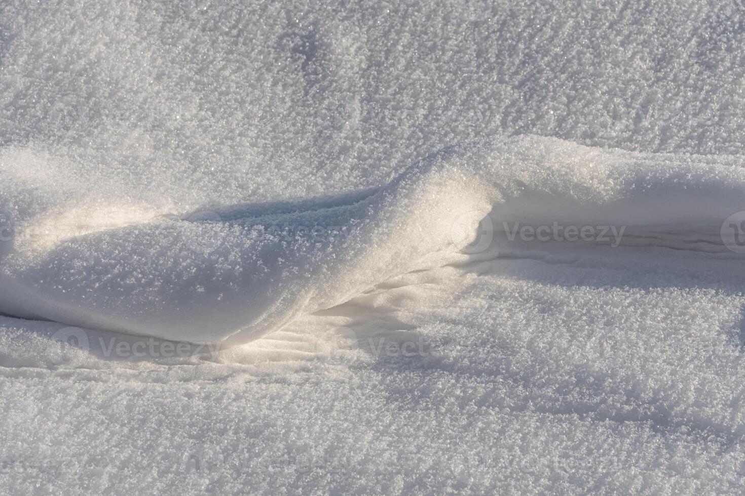 A fun small snowdrift of white snow with yellow sunshine and bokeh light at sunset on a blurred background in a park in winter photo