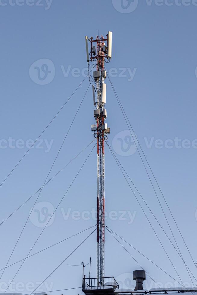 Gray metal cell tower carrying antennas of cellular networks on the blue sky with white clouds background in sunny day. Vertical photo