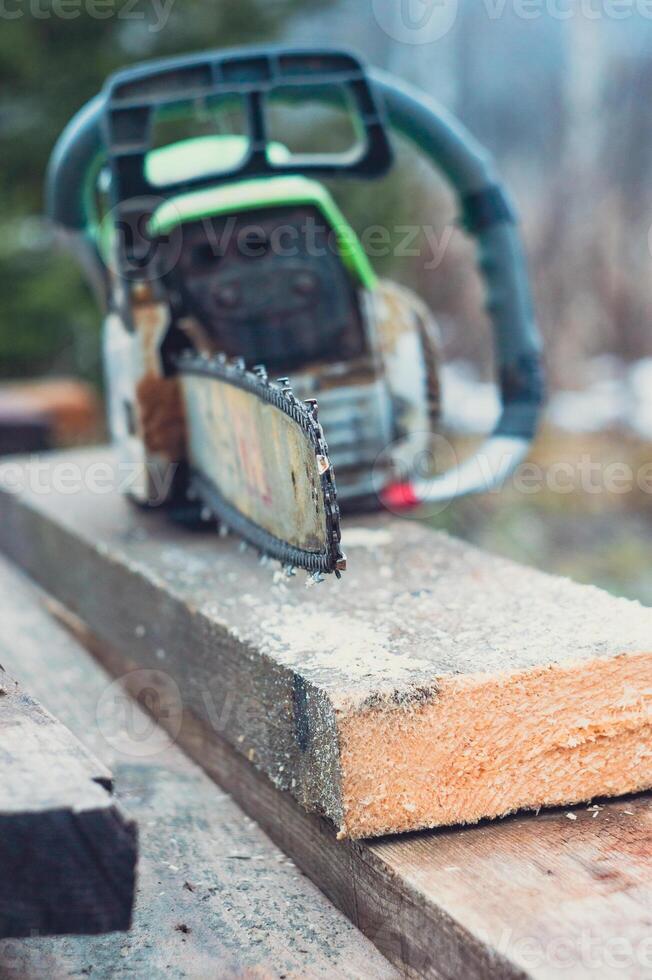 An old working chainsaw is lying on a sawn board fifty millimeters. Photos on the street in the yard for ideas for building from wood and planks. High quality photo