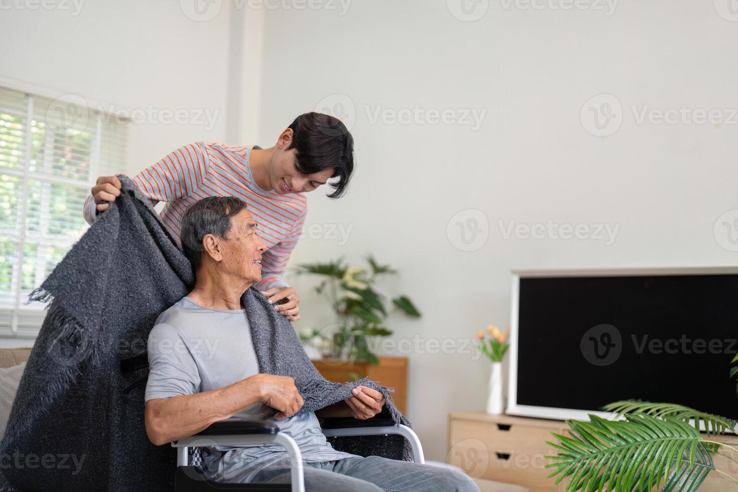 Son covering elderly father with a blanket in wheelchair at home. photo