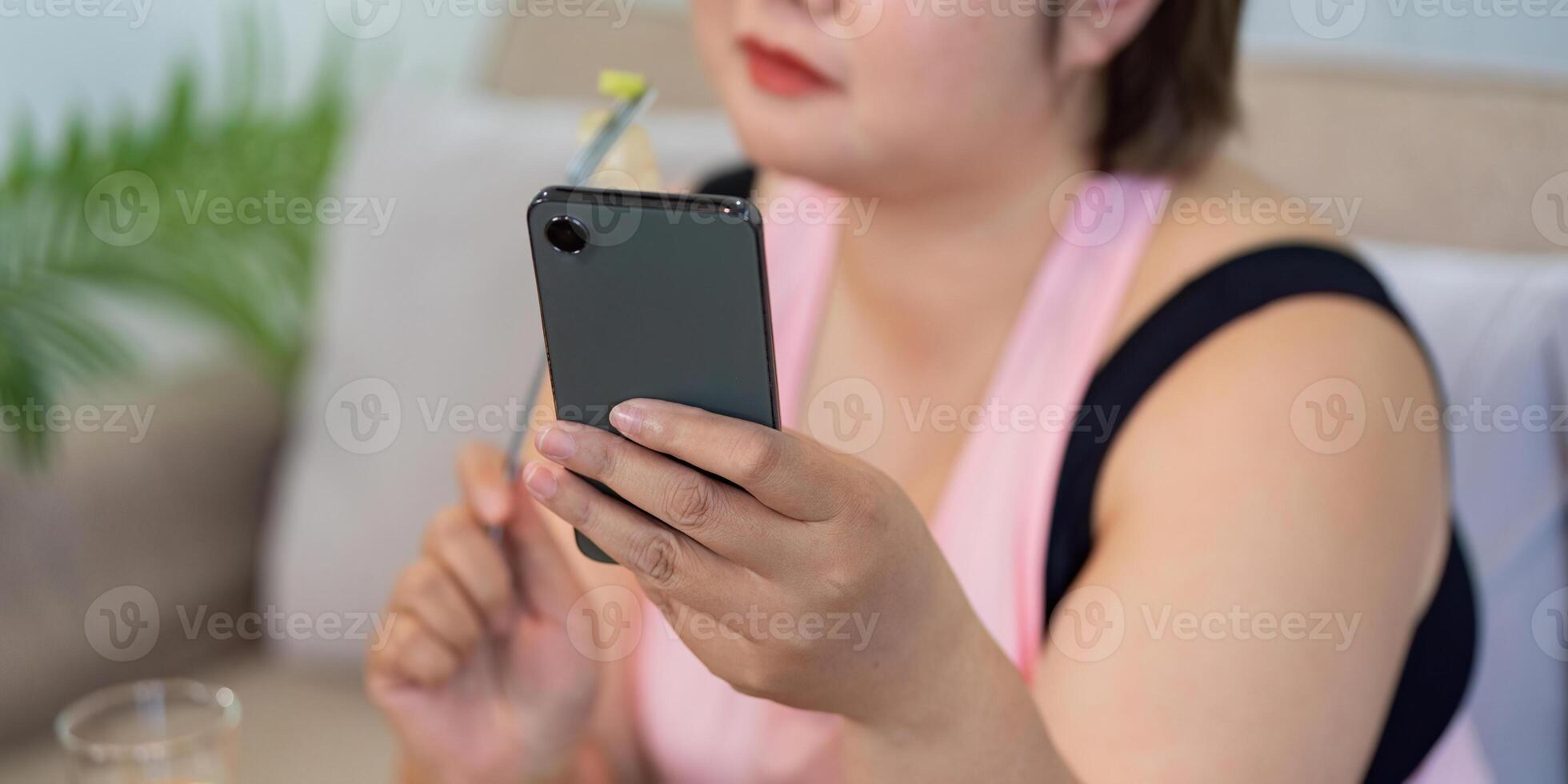 Overweight woman using smartphone while enjoying a healthy meal at home, focusing on weight loss. photo