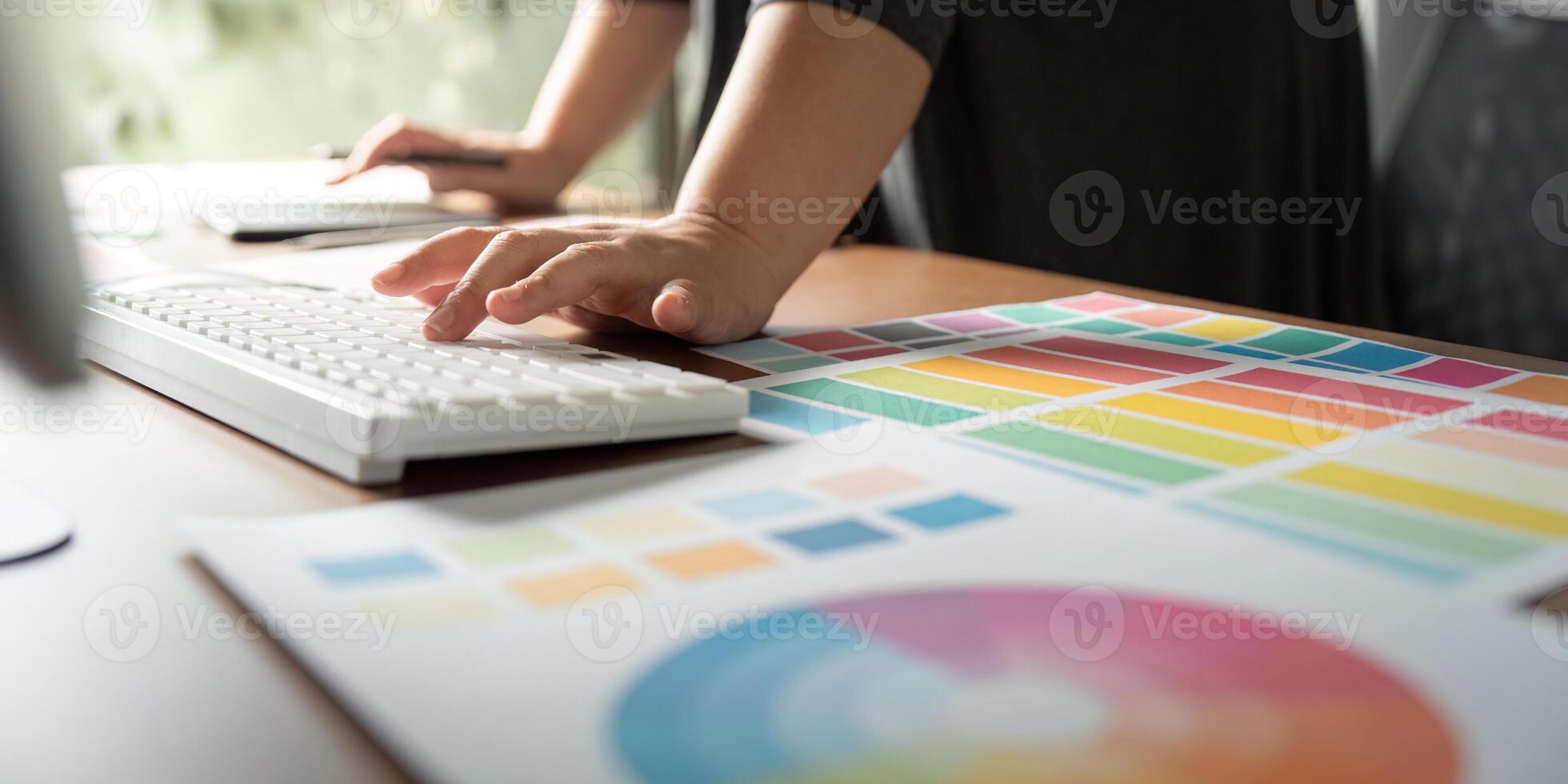 Graphic designer working on a computer keyboard with color charts at a creative desk. photo