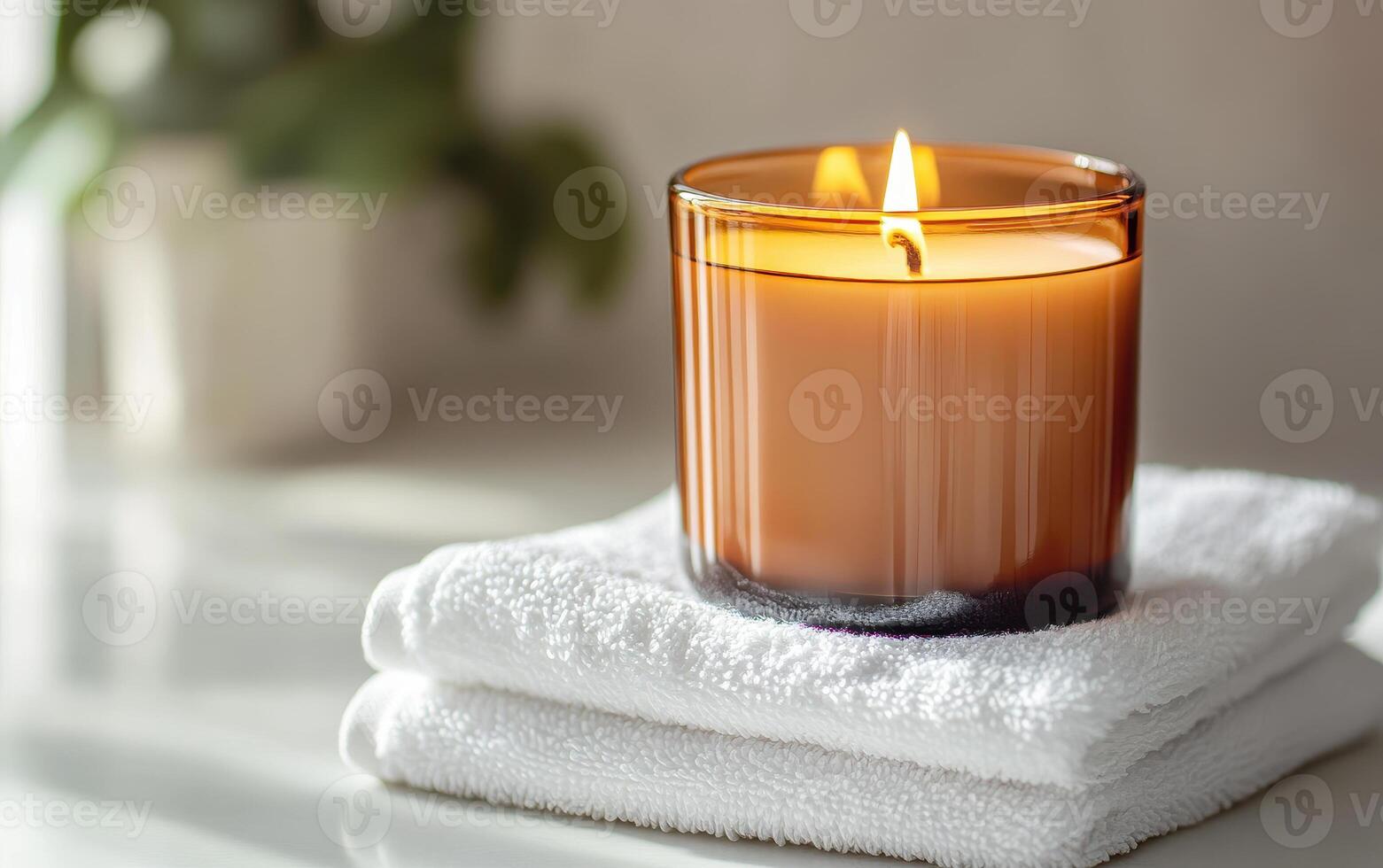 warm amber jar candle sits atop stack of soft white towels, creating serene and inviting atmosphere. flickering flame adds touch of tranquility to setting photo