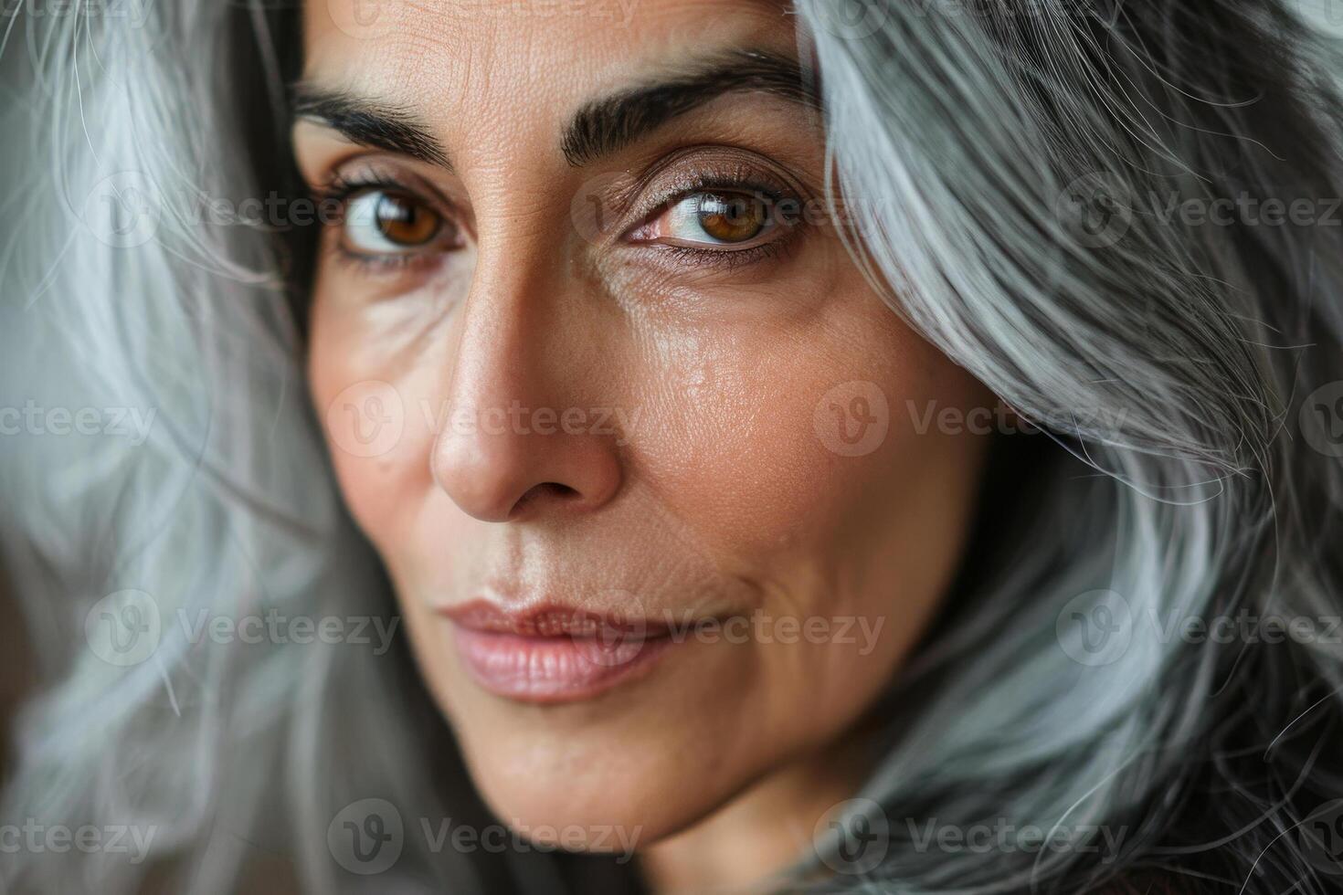 This portrait features a woman with captivating gray hair and expressive brown eyes, radiating confidence and serenity in warm, natural light photo