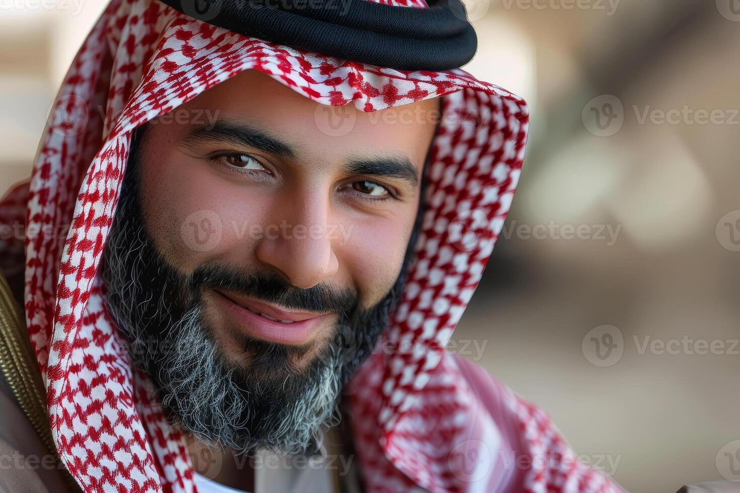 A man dressed in traditional attire smiles warmly while posing for a portrait. The background reveals elements of a cultural event, filled with lively energy photo