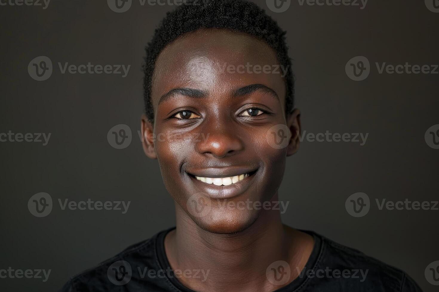 A young man with a bright smile is standing in front of a dark background, showcasing confidence and warmth. His casual attire adds to the friendly atmosphere photo
