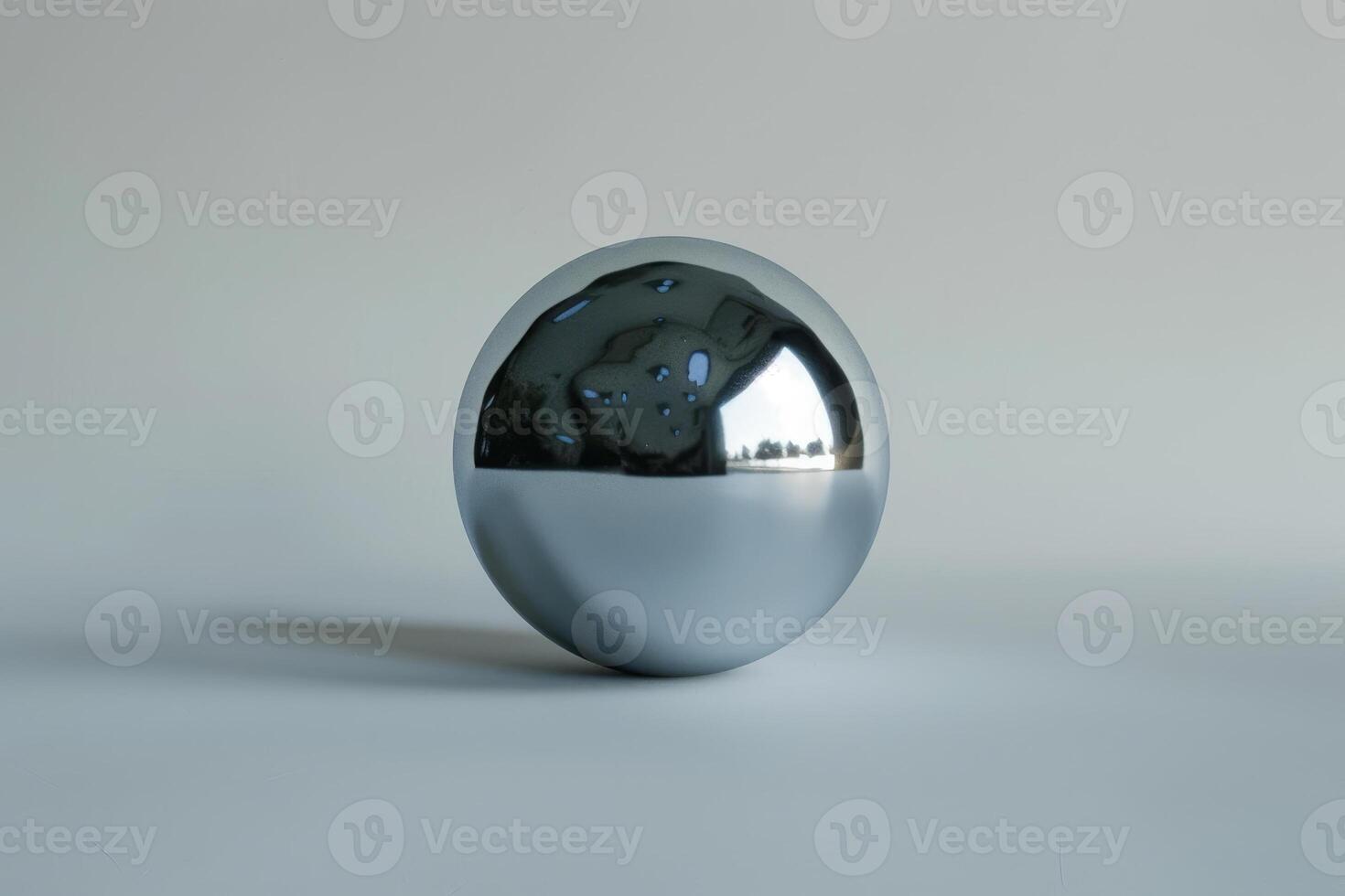 A polished, reflective metallic sphere is placed on a smooth, neutral surface, demonstrating modern design. The sphere mirrors its surroundings, creating an intriguing visual contrast photo