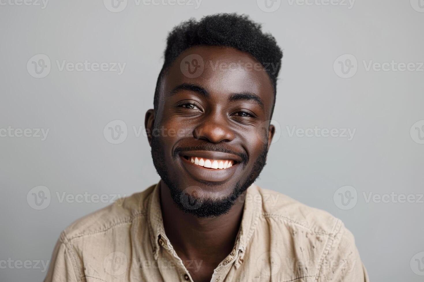 A young man with a bright smile sits against a gray background, dressed in casual attire, exuding happiness and warmth in a relaxed studio environment photo