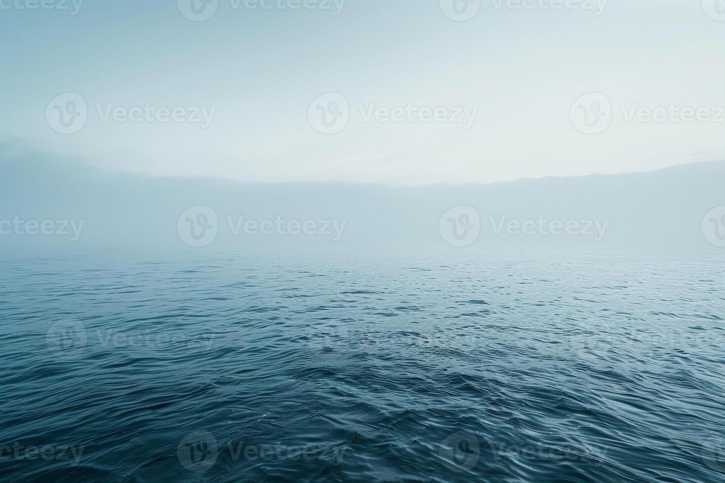 The serene seascape features gentle waves reflecting the soft hues of dawn, enveloped in a mist that creates a peaceful atmosphere over the water photo