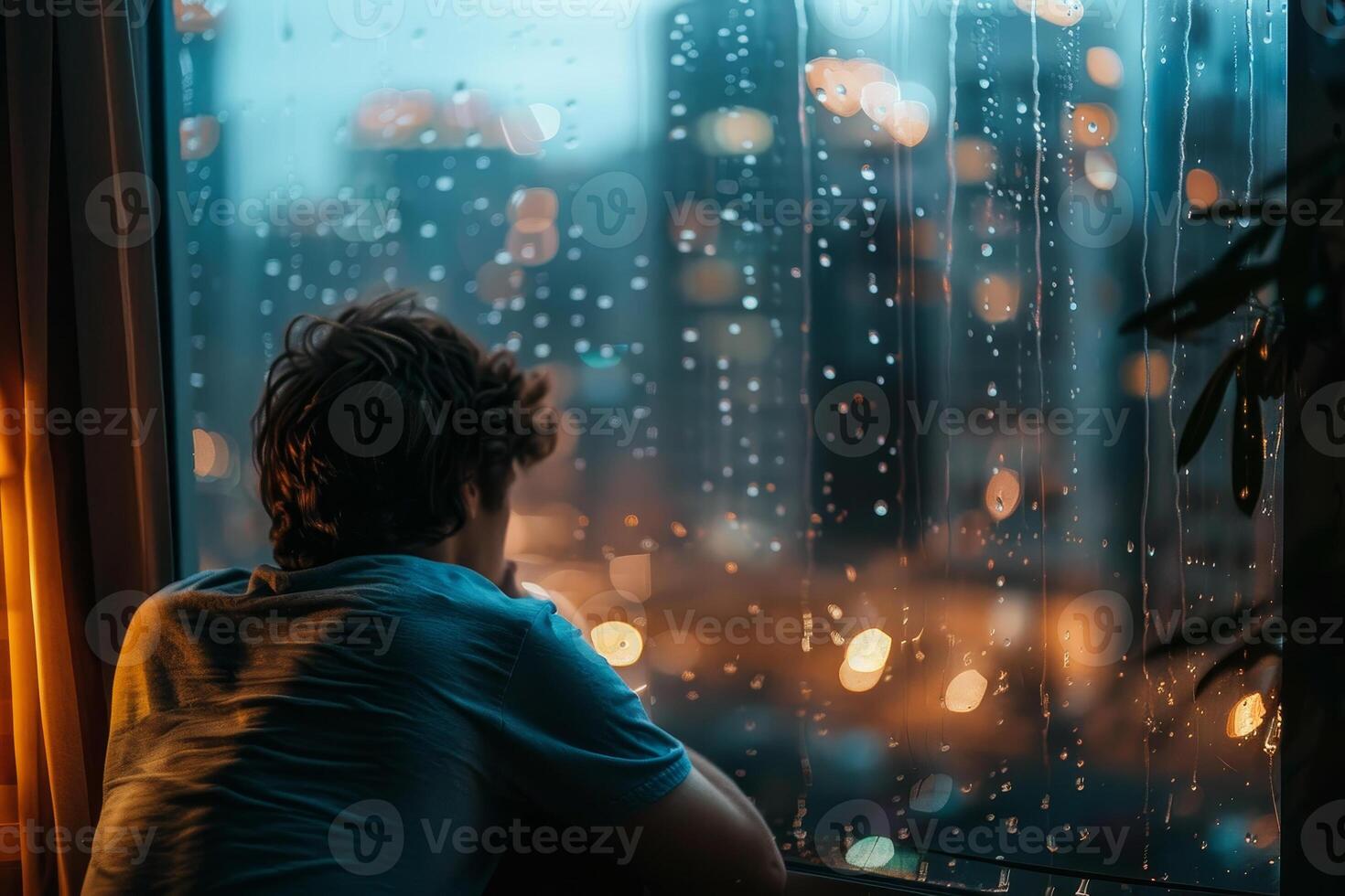 A man sitting in front of a window looking out at the rain photo