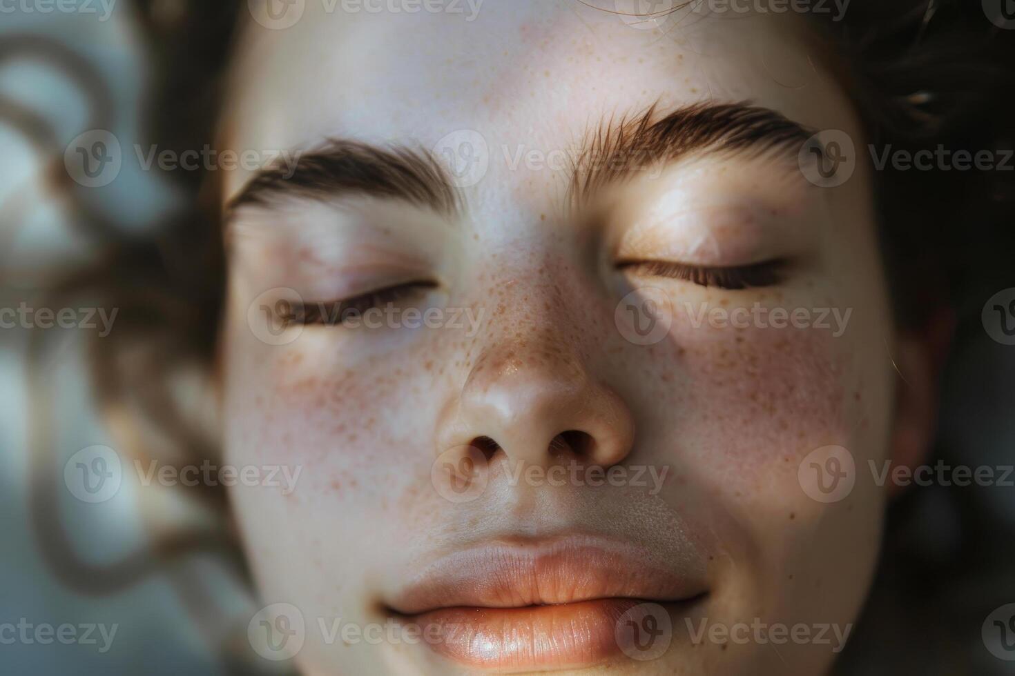 A woman with brown hair and freckles is smiling and resting her head on her hand photo