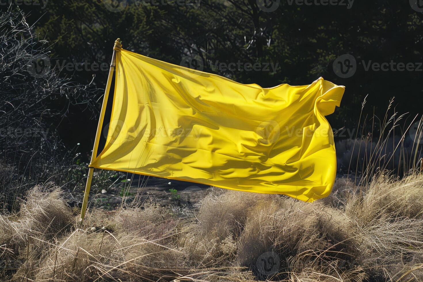 A bright yellow flag stands tall, fluttering in the wind amidst dry grass and scattered greenery, capturing the essence of a sunny day outdoors photo