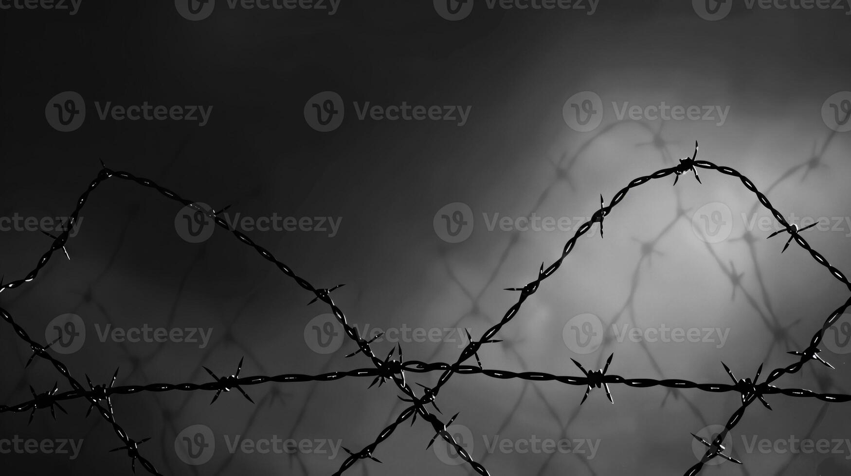 A black and white photo of a barbed wire fence with a dark sky in the background