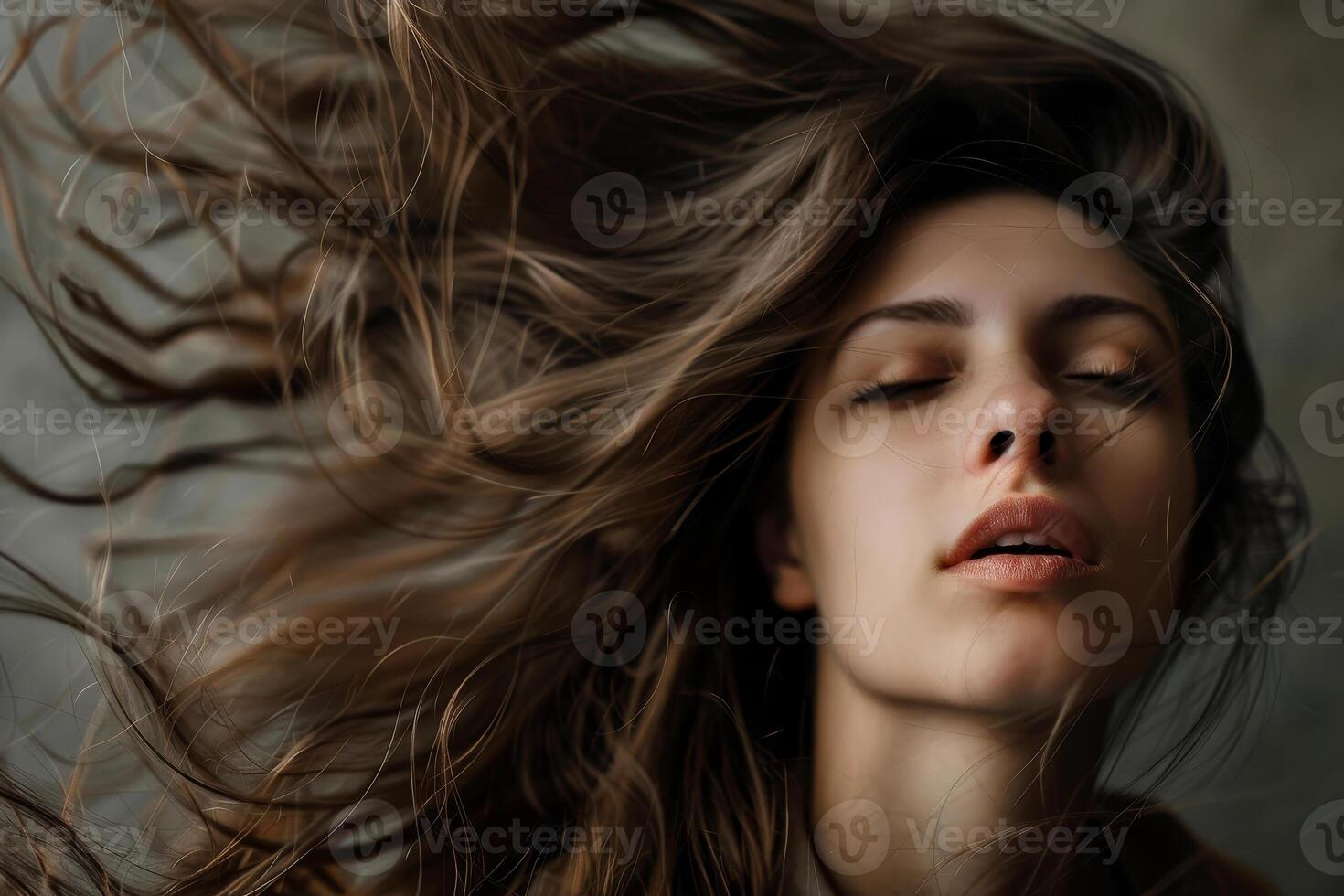 A young woman with long, flowing hair tilts her head back, eyes closed, savoring a peaceful moment against a muted backdrop, embracing tranquility and reflection photo