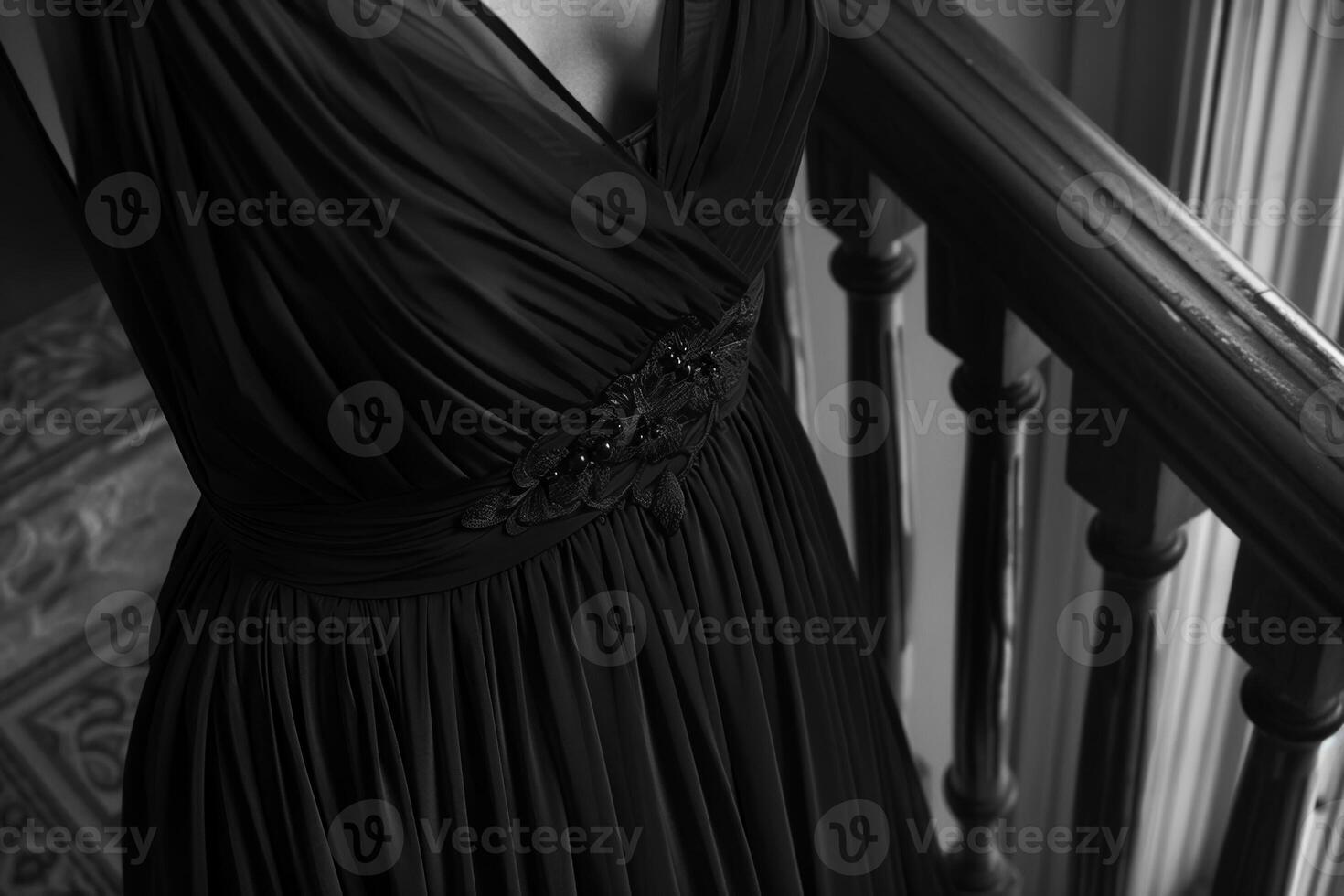 A person stands on a staircase, showcasing a flowing black dress that gently drapes over the railing. The interior is warmly lit, highlighting the elegant fabric photo