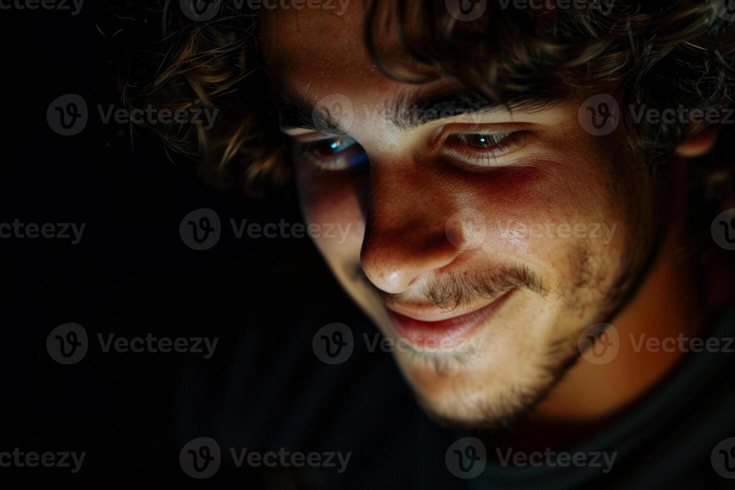 The young man appears engaged and happy as he explores content on his smartphone in a cozy, low-light environment, creating an intimate atmosphere photo