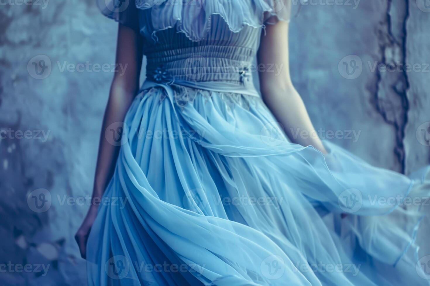The woman stands elegantly, her delicate blue dress billowing gently around her. The soft fabric contrasts beautifully with the textured gray wall behind her, creating an enchanting mood photo