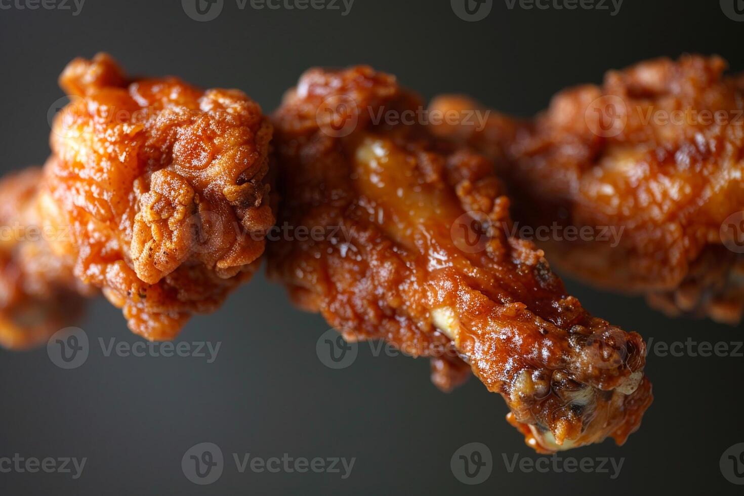 Crispy fried chicken wings are suspended in front of a dark backdrop, showcasing a rich, glossy sauce that enhances their delicious appearance photo