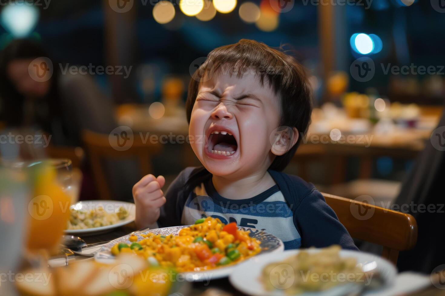 A young boy is screaming at a table with food photo