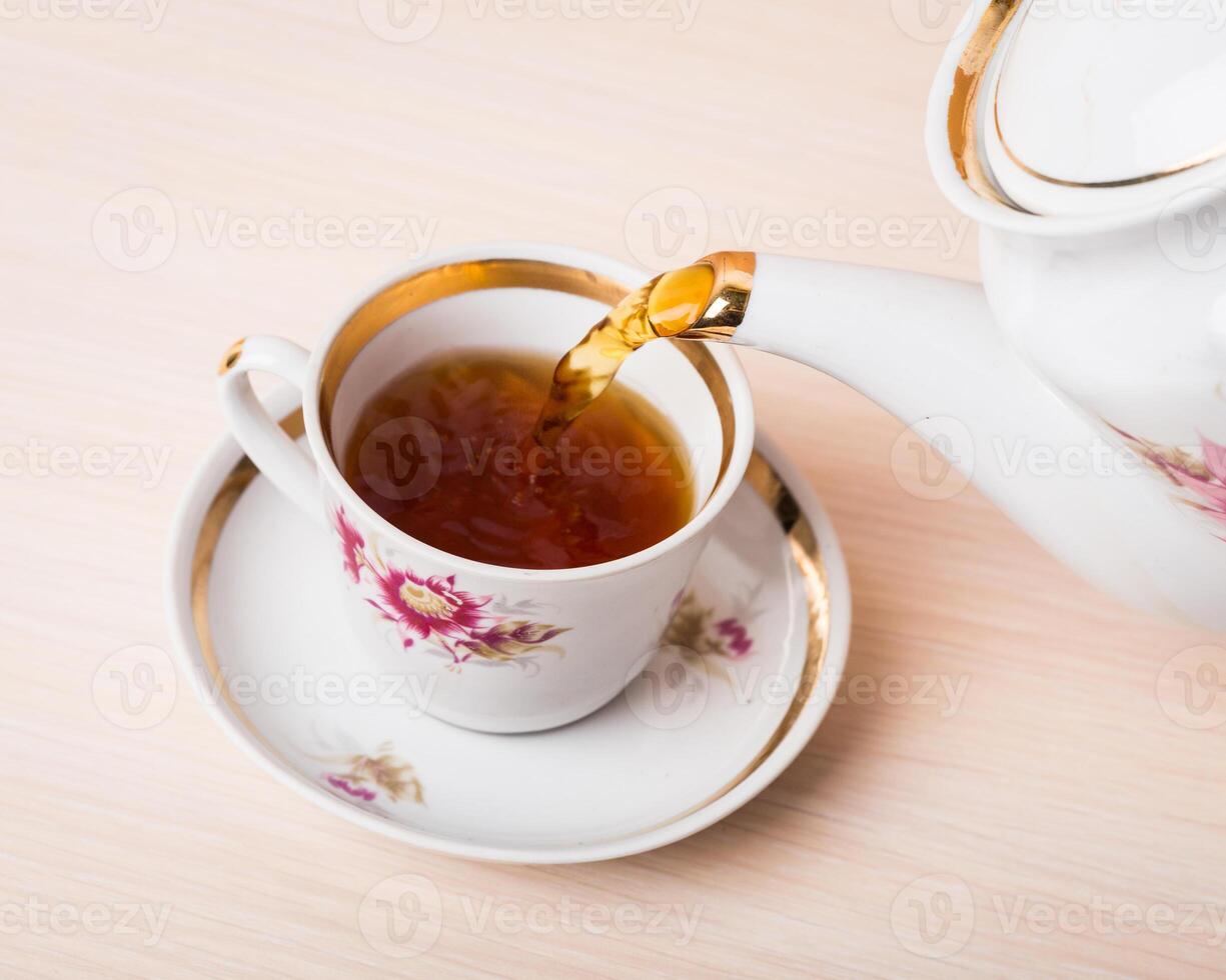 Old-style porcelain kettle pouring tea from jug to cup of tea photo