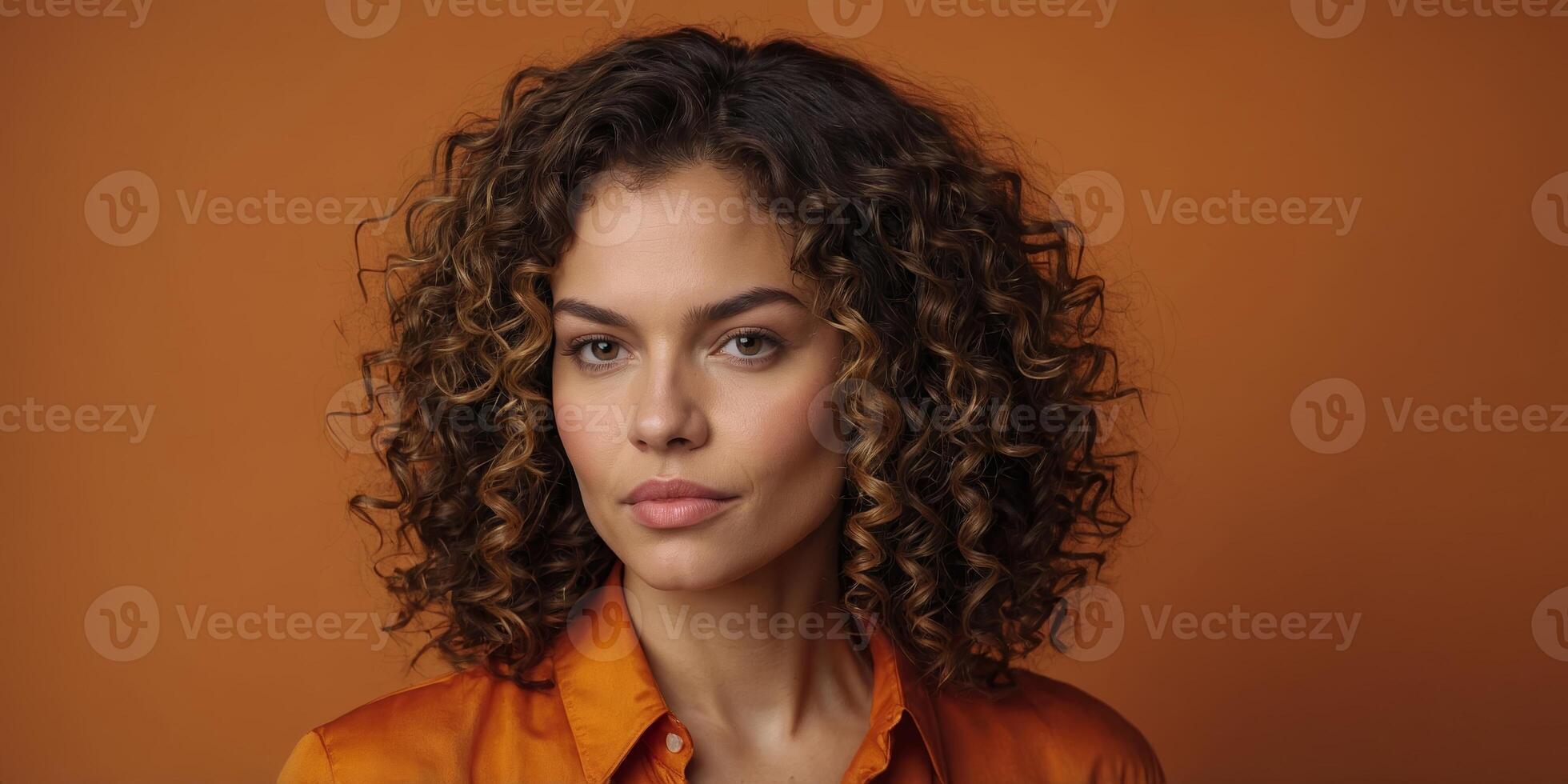 Portrait of a woman with curly hair wearing an orange shirt against a warm backdrop photo