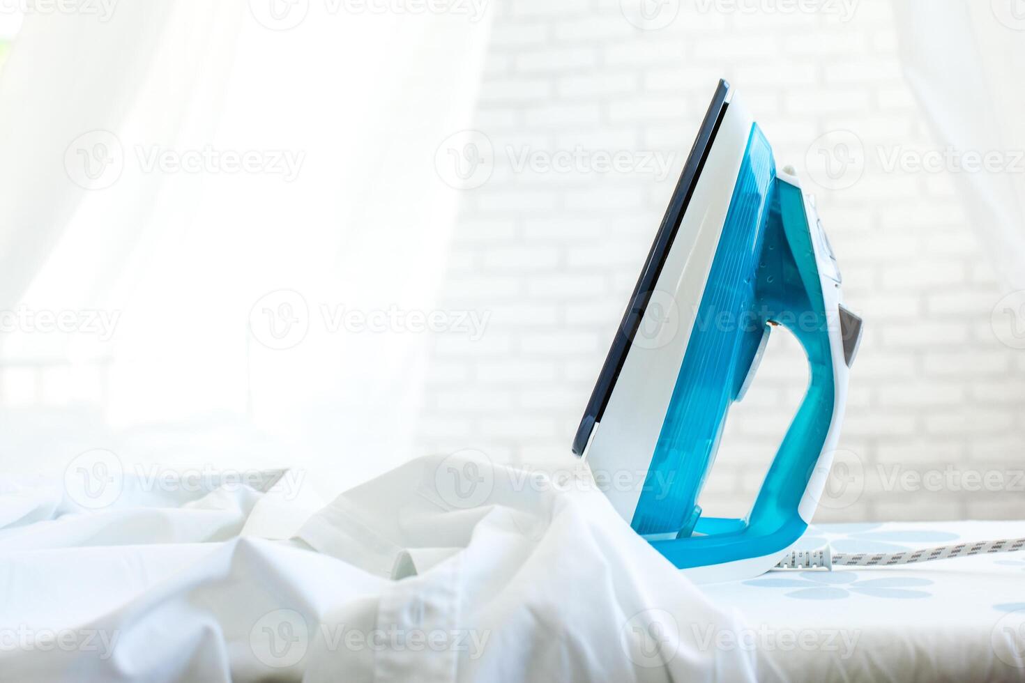 Iron on ironing board on light home interior background photo