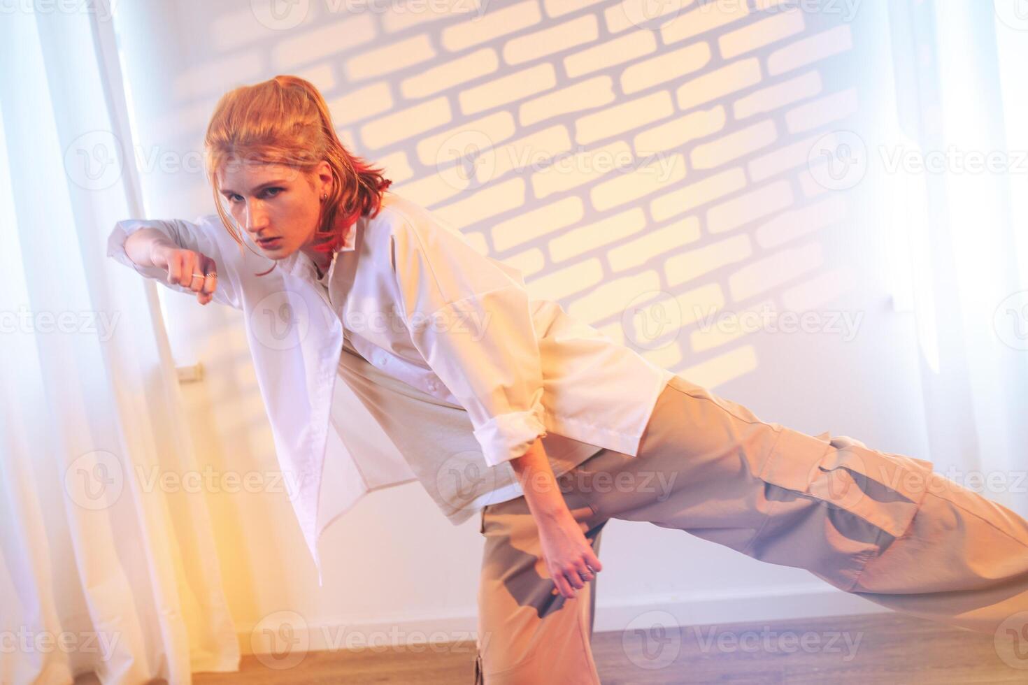 Young model in casual streetwear poses dramatically in a studio with soft lighting and textured wall backdrop photo