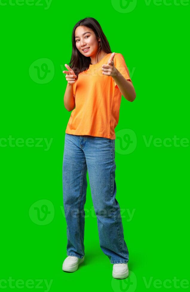 Young woman poses playfully in orange shirt and jeans against bright green background photo