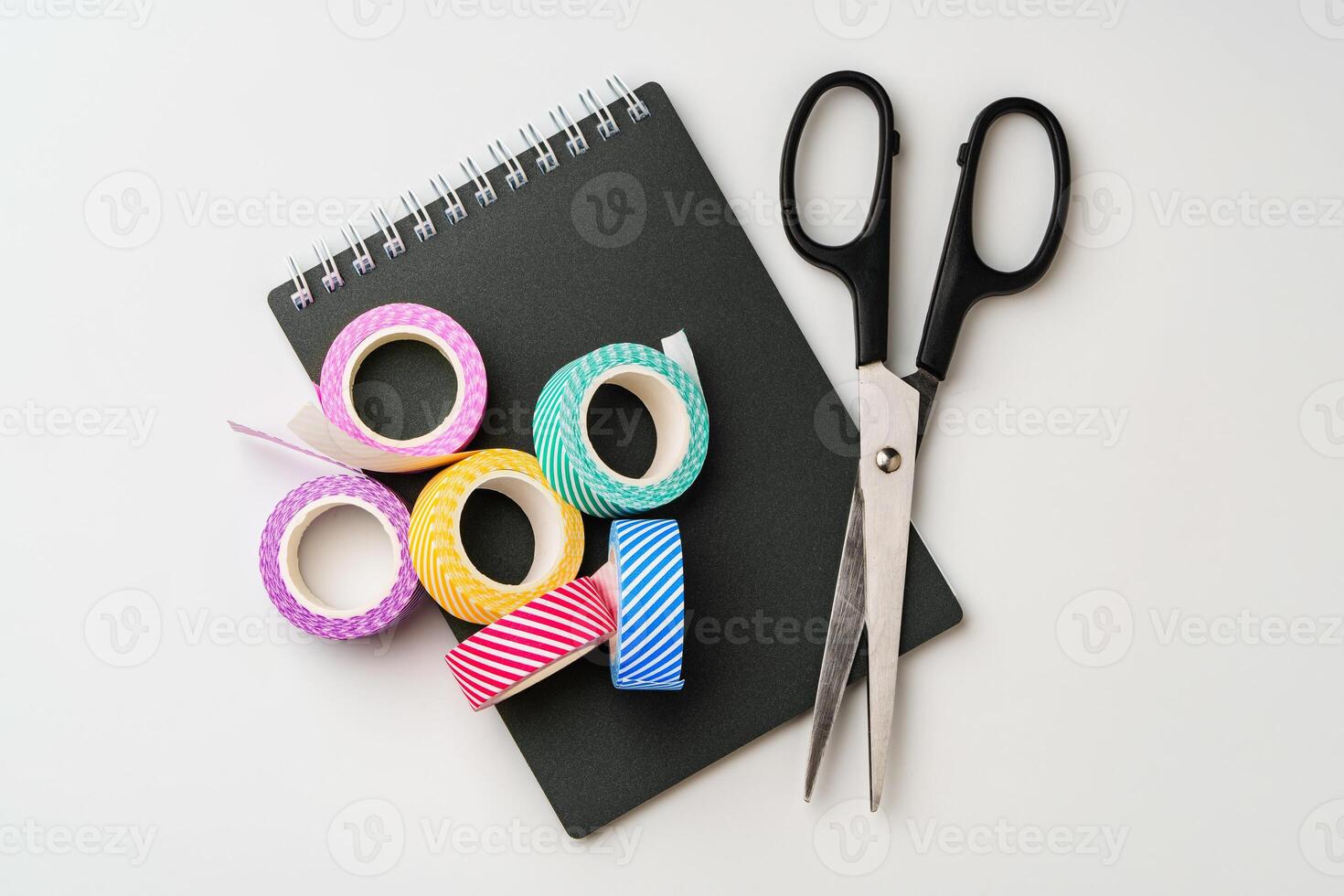 Crafting essentials on a workspace featuring colorful tape and scissors beside a notepad photo