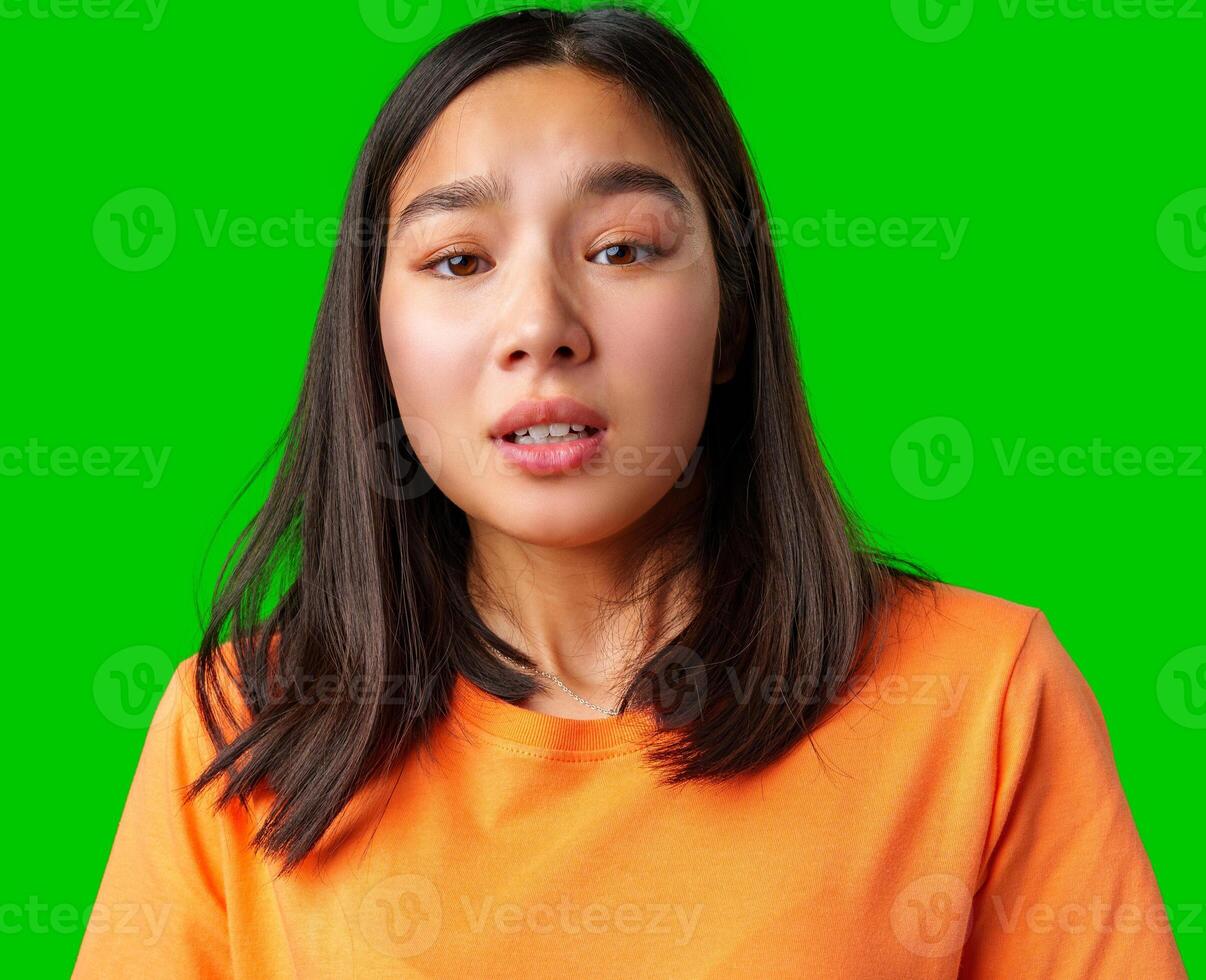 Young woman with expressive face wearing orange shirt and standing against green backdrop displays a range of emotions in a vibrant setting photo