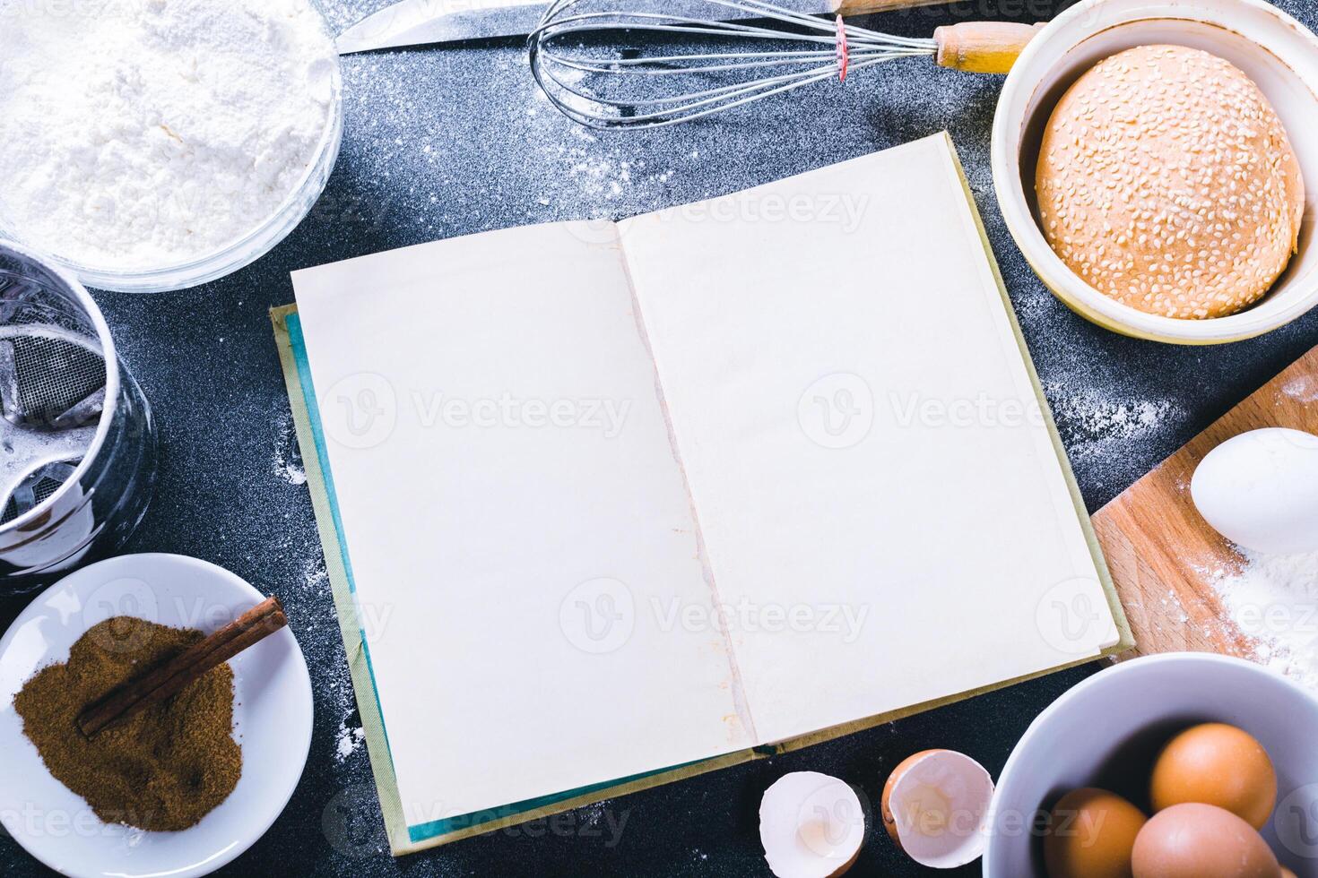 Baking dark background with blank cook book, eggshell, bread, flour, rolling pin. Ingredients for the baking. photo