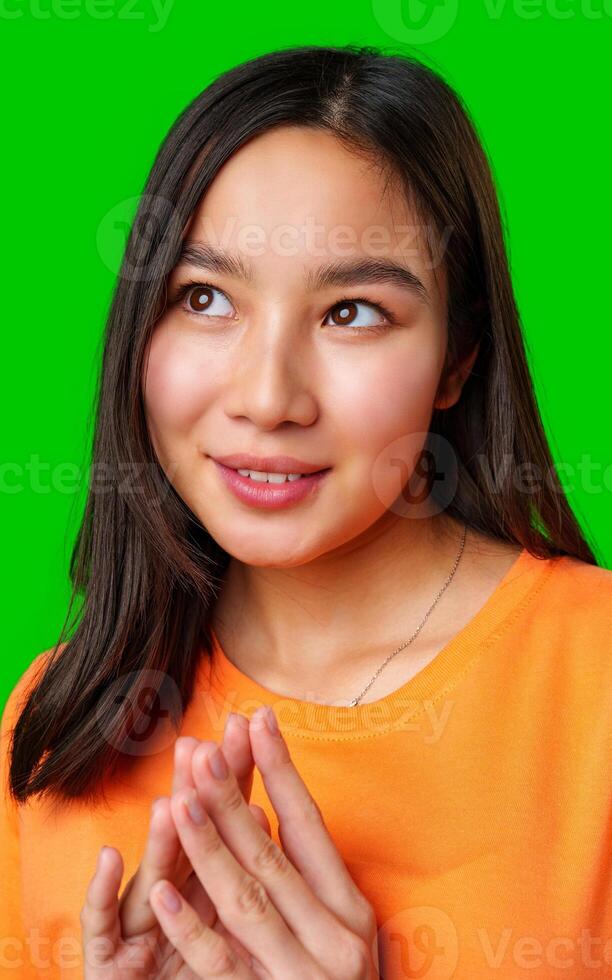 Young woman in orange shirt smiling and expressing curiosity against a green background photo