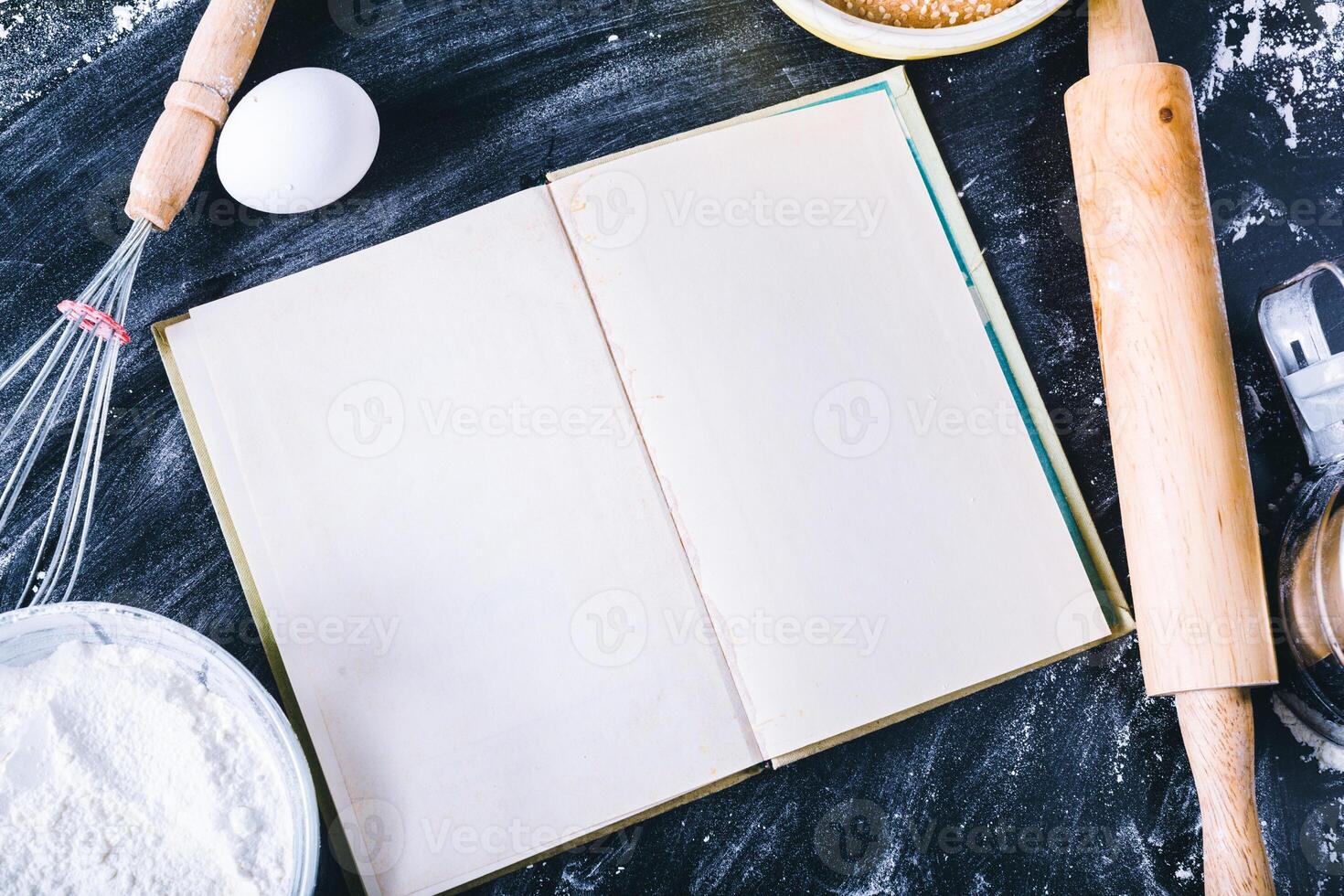Baking dark background with blank cook book, eggshell, bread, flour, rolling pin. Ingredients for the baking. photo