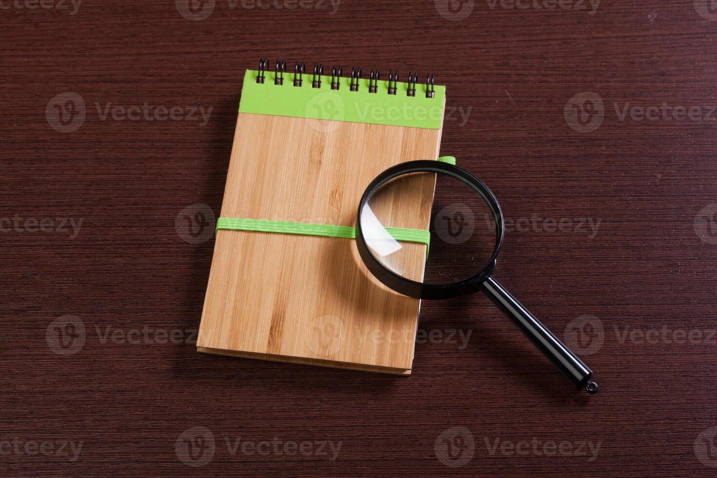 Notebook and magnifier on a wooden background photo
