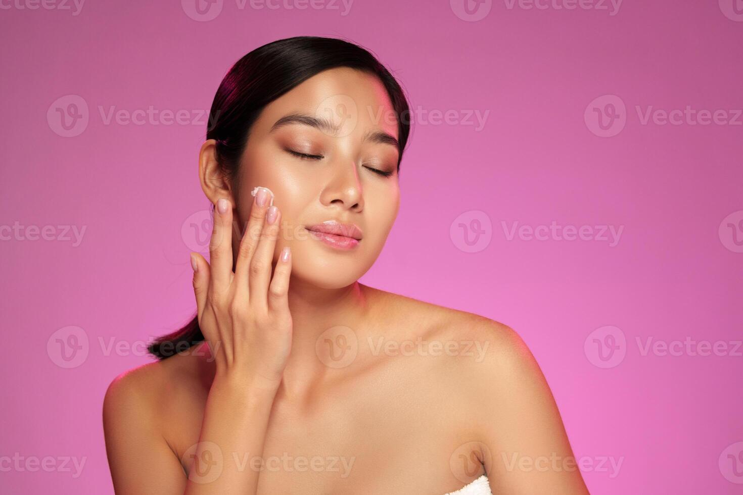 Woman applying skincare product with a gentle touch in a brightly lit studio during a beauty session photo