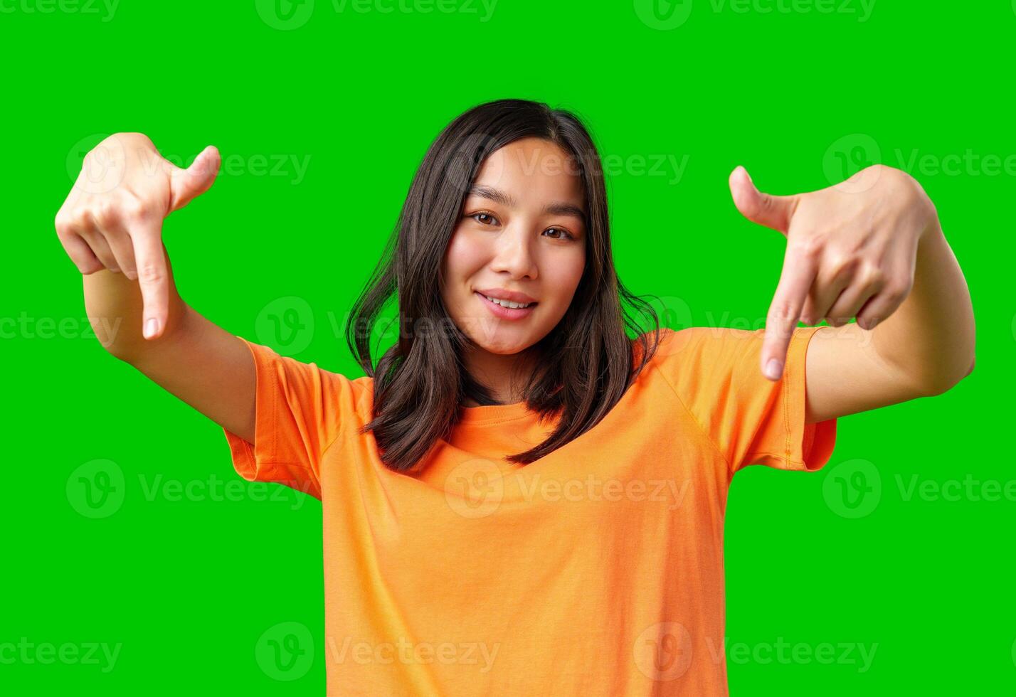 Young woman in orange shirt gestures playfully against bright green backdrop while smiling and having fun photo