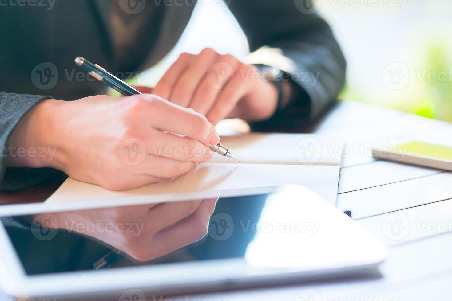 Professional man writes notes on paper while using a tablet at a modern workspace in daylight photo