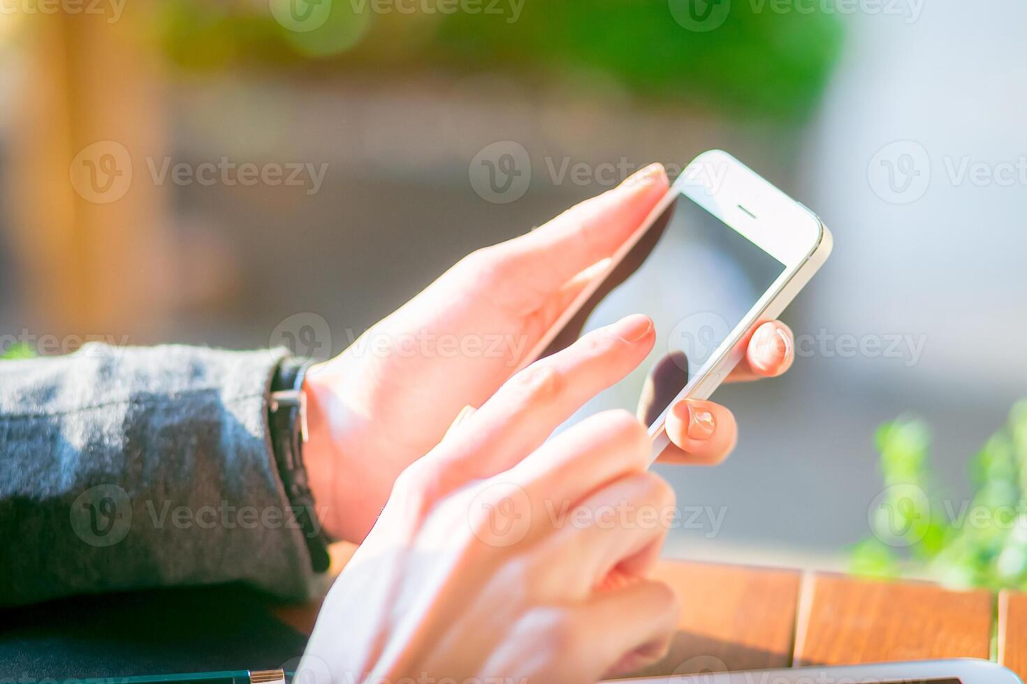 Person using smartphone outdoors in a sunny setting while sitting at a table photo