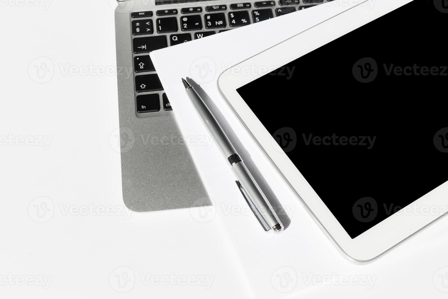 Workspace setup featuring a tablet, laptop, pen, and documents on a clean surface in a modern office environment photo