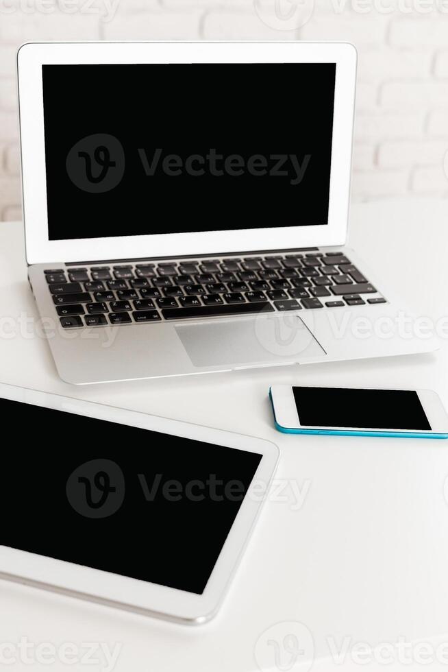 Modern workspace with laptop, tablet, and smartphone on white table in bright room photo