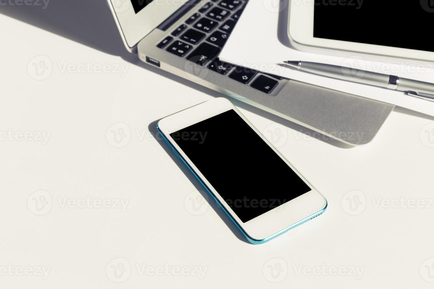 Smartphone placed next to laptop and tablet on a clean white desk during a productive work session photo