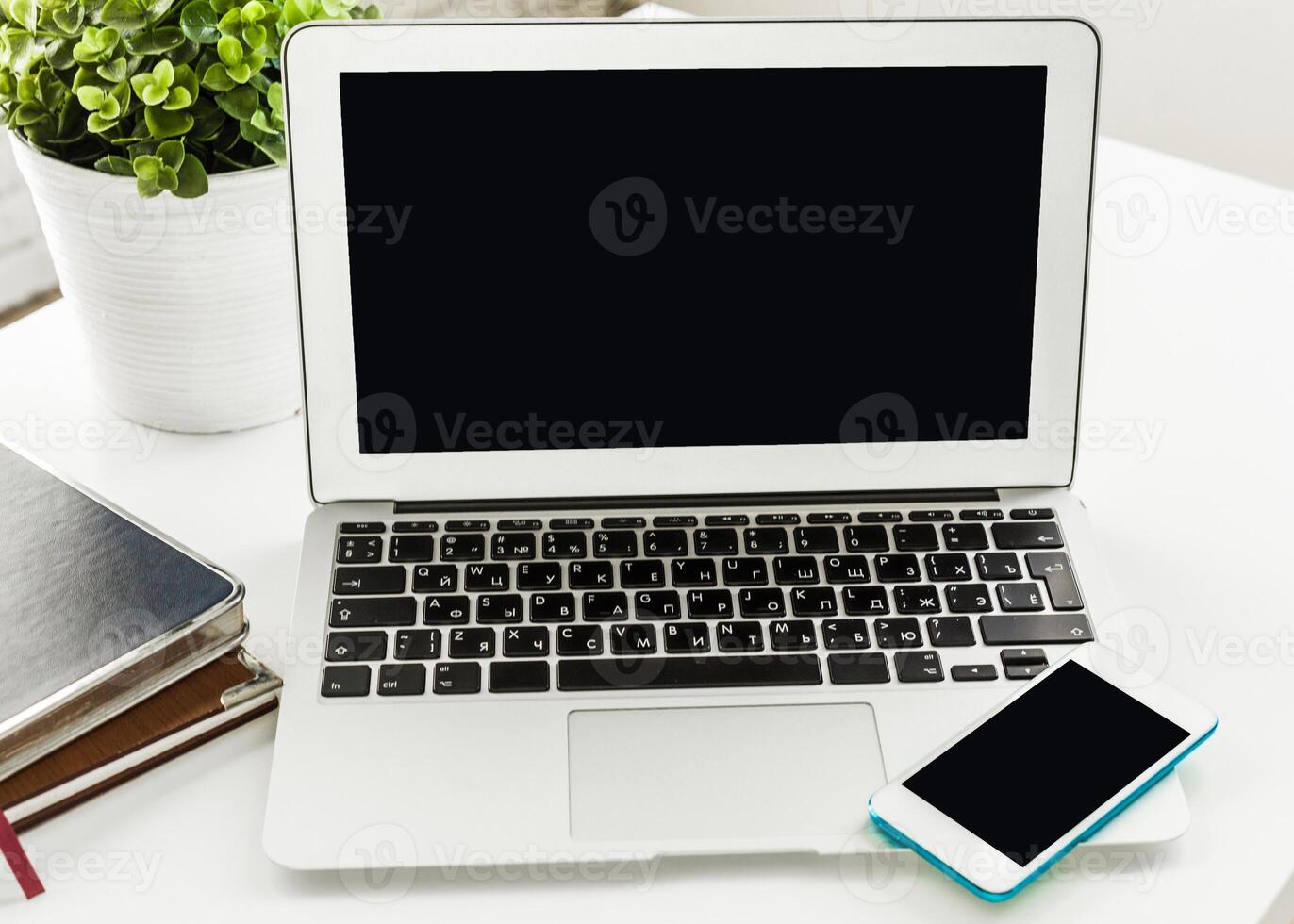 Workspace setup with a laptop, smartphone, and a plant in a bright, modern office environment photo
