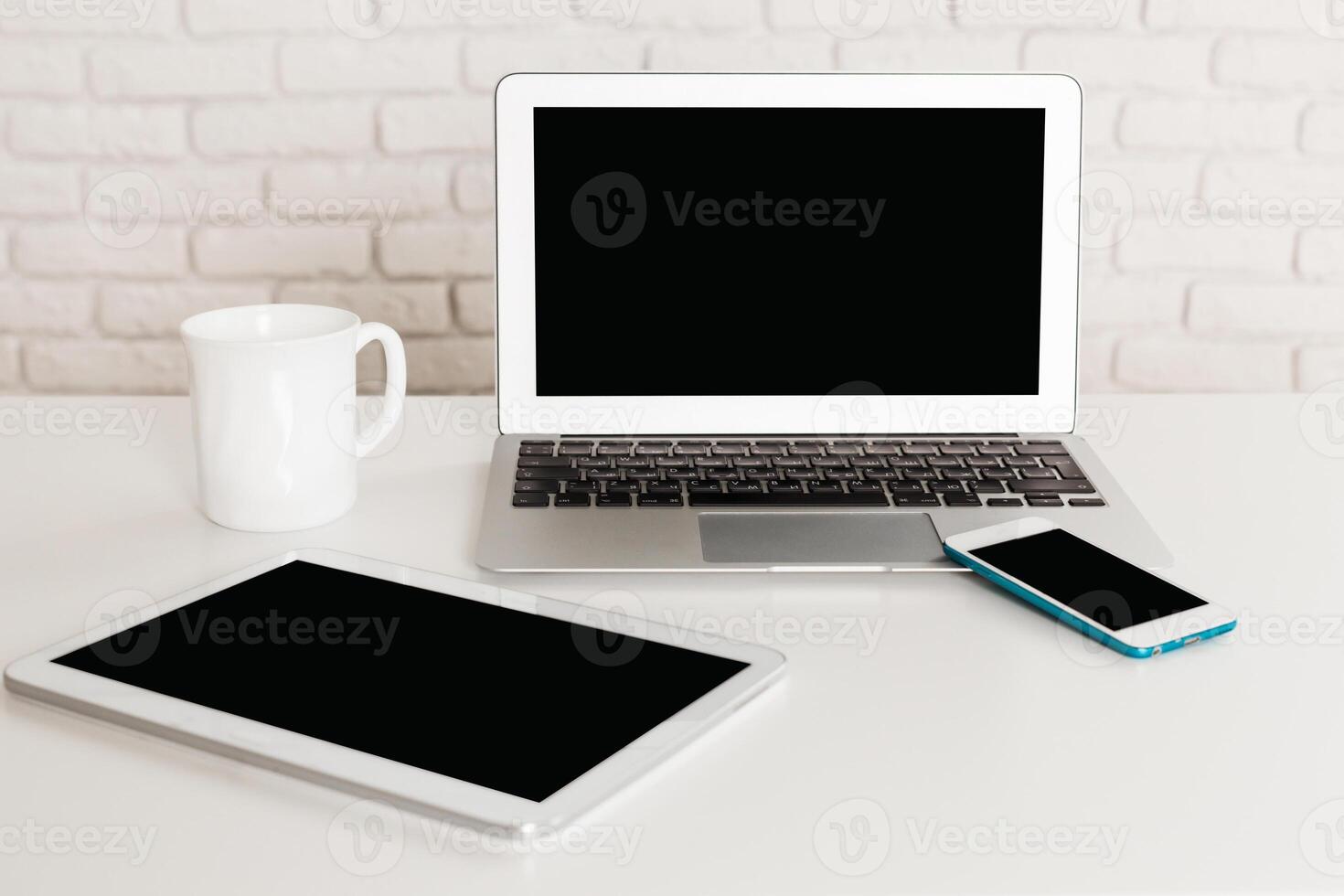 Desk setup with laptop, tablet, smartphone, and mug in a minimalist environment photo