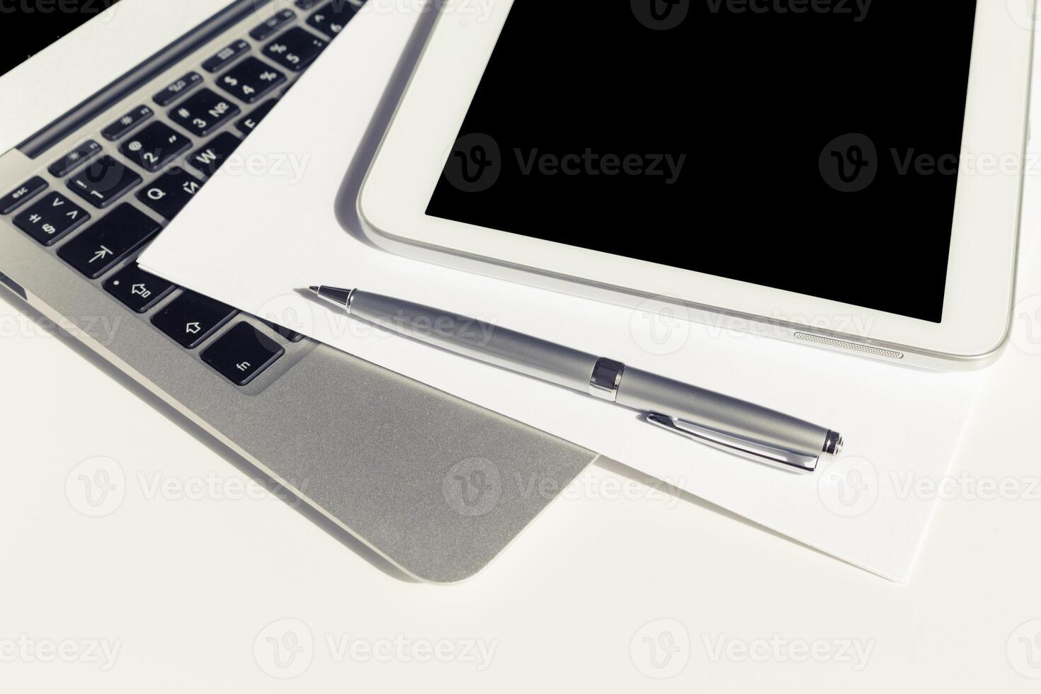 Workspace arrangement with laptop, tablet, pen, and blank paper on desk for creative and productive tasks photo
