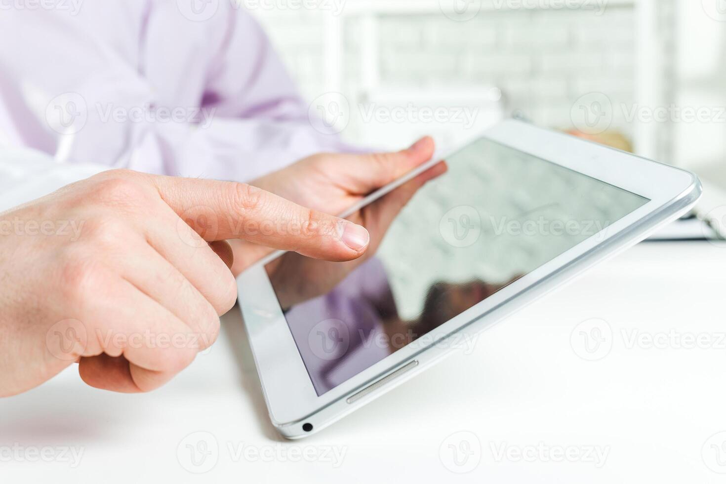 Person interacting with a tablet device while seated at a desk in a bright, modern workspace photo