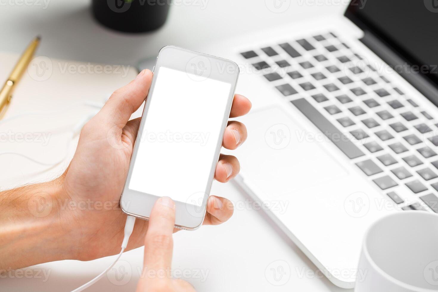Engaging with a smartphone while sitting at a workspace with a laptop and stationery items photo