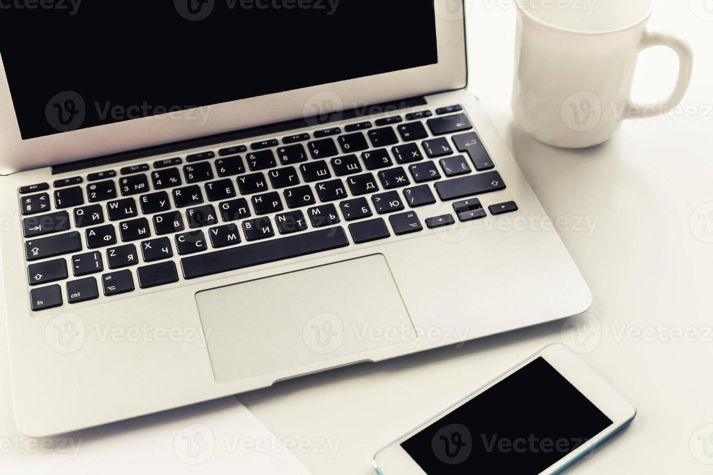 Workspace setup with laptop, smartphone, and coffee cup on a white desk during morning hours photo
